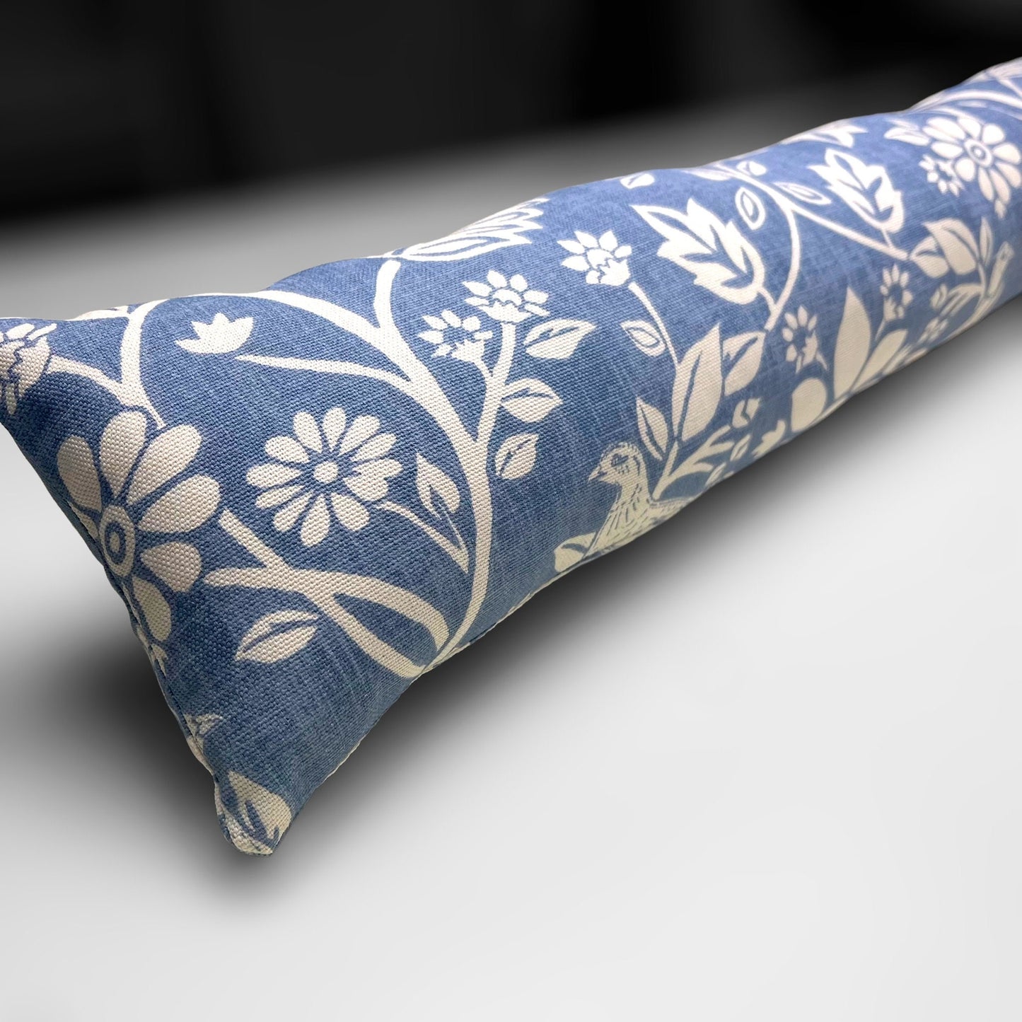 Handmade Blue Woodland Hares draught excluder with a deep blue fabric featuring white hare motifs, placed against a door to block cold air.