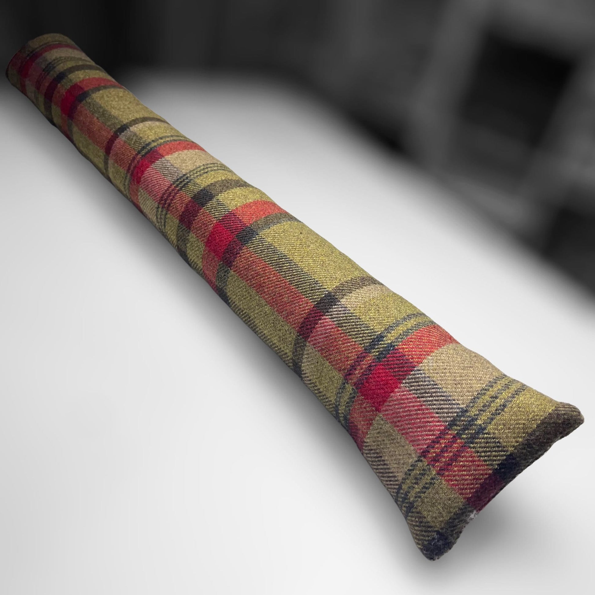 Handmade wool tartan draught excluder in green, red, and brown tones, designed to block drafts under doors.