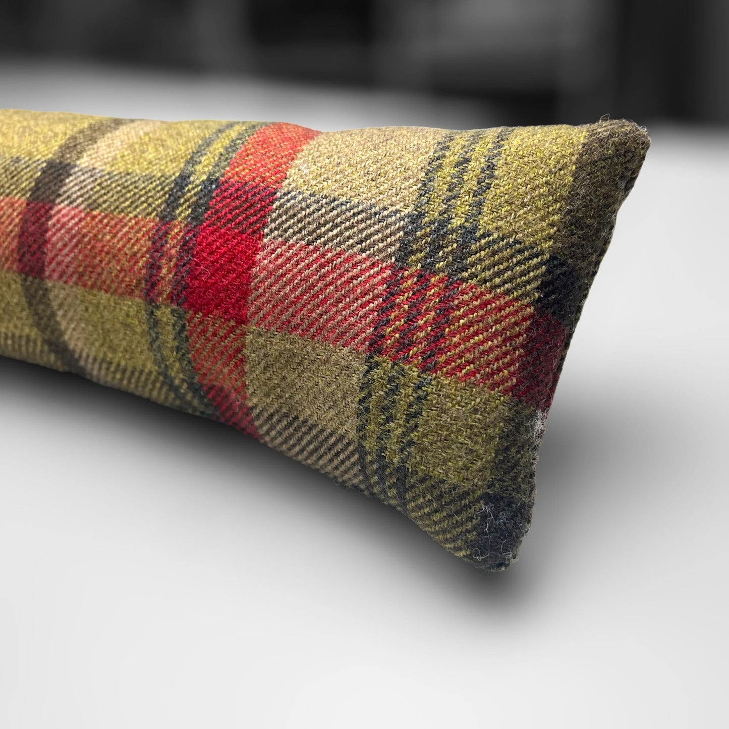 Handmade wool tartan draught excluder in green, red, and brown tones, designed to block drafts under doors.