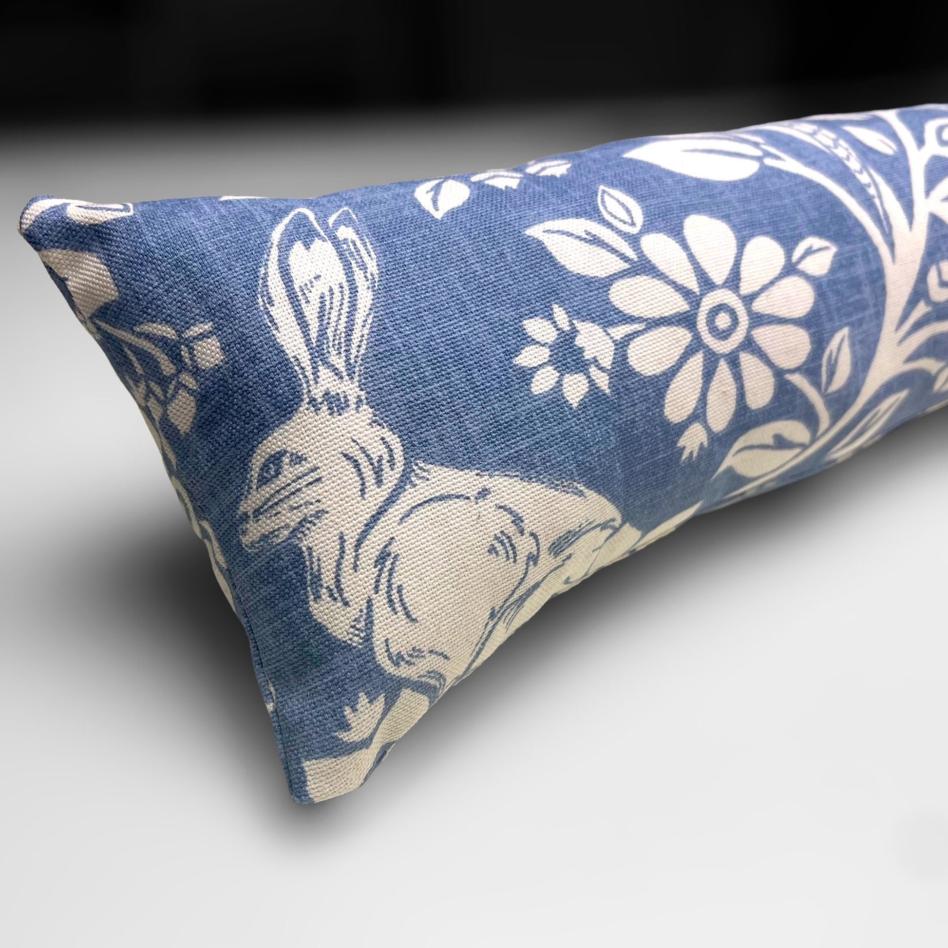 Handmade Blue Woodland Hares draught excluder with a deep blue fabric featuring white hare motifs, placed against a door to block cold air.