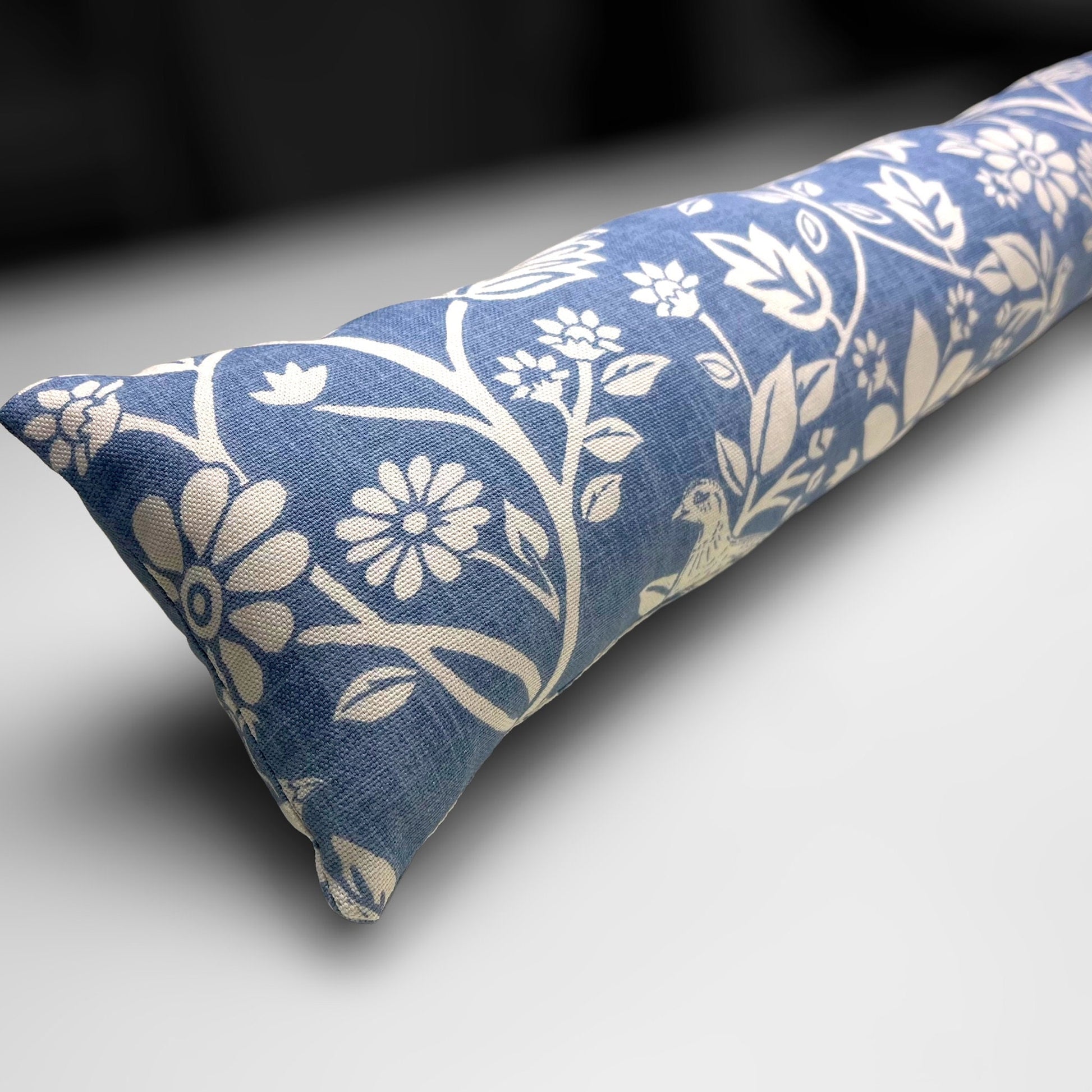 Handmade Blue Woodland Hares draught excluder with a deep blue fabric featuring white hare motifs, placed against a door to block cold air.