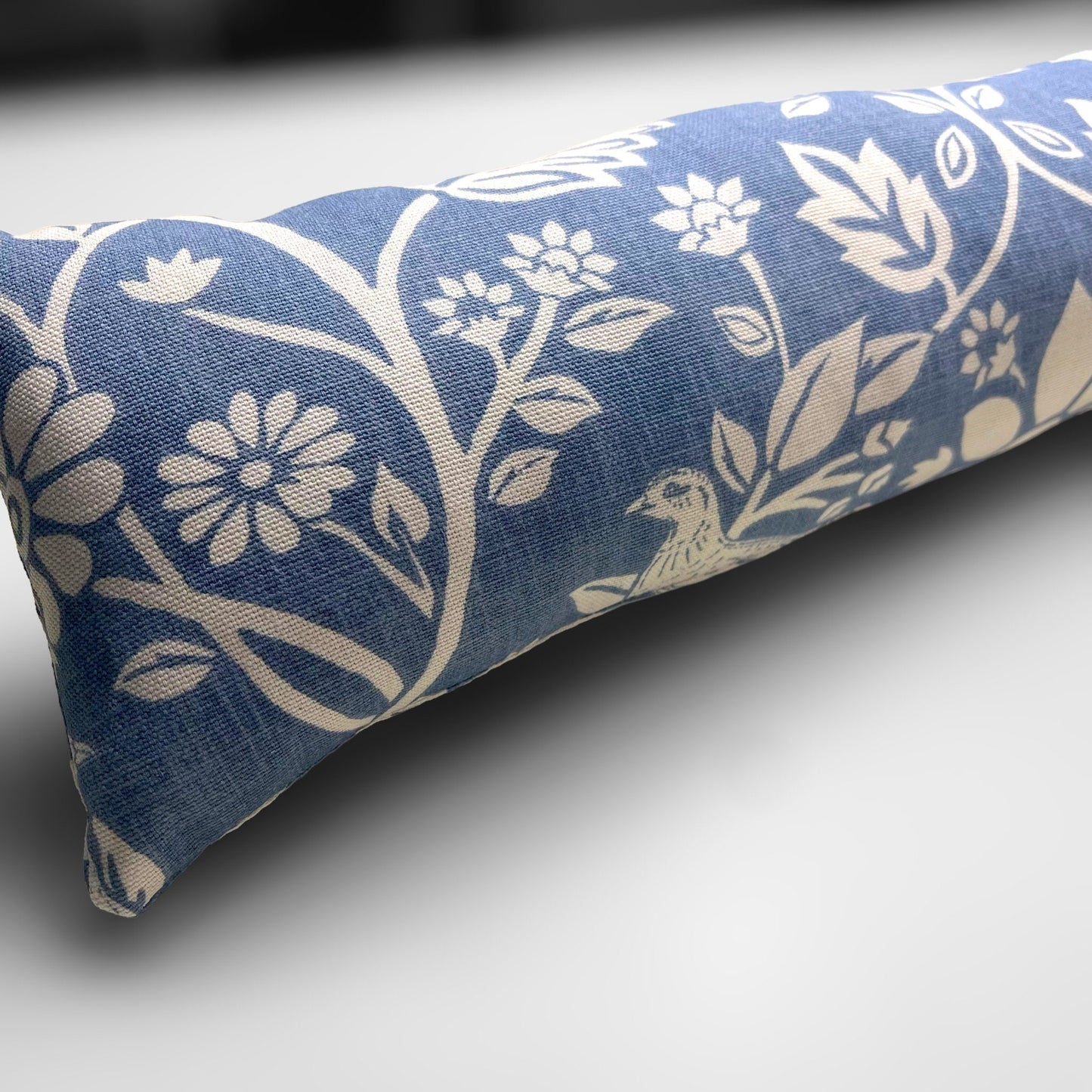 Handmade Blue Woodland Hares draught excluder with a deep blue fabric featuring white hare motifs, placed against a door to block cold air.