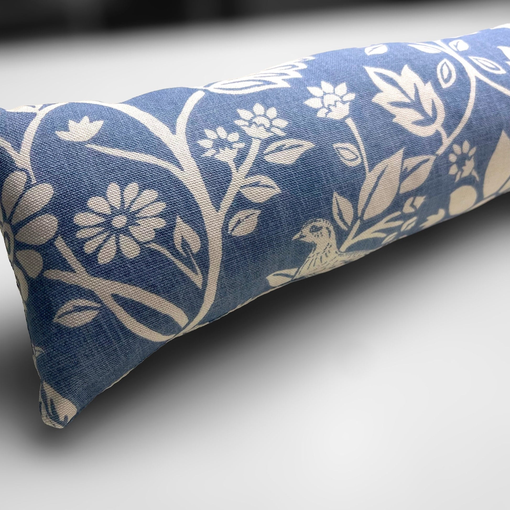 Handmade Blue Woodland Hares draught excluder with a deep blue fabric featuring white hare motifs, placed against a door to block cold air.